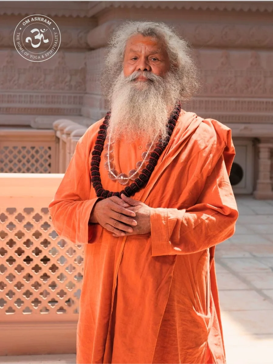 Beloved Gurudev standing before the intricately carved stone Shiva Temple at OM Ashram, inviting practitioners to Yoga Day.
